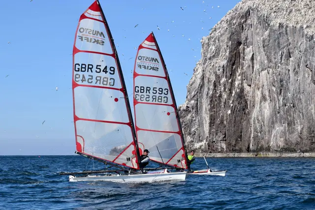 Dwie łódki Musto Skiff ścigające się pod skałą Bass Rock przy North Berwick